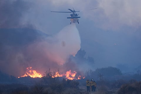 A helicopter drops water on the Hughes Fire