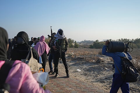 Hamas fighters stand on a road as displaced Palestinians return to Gaza
