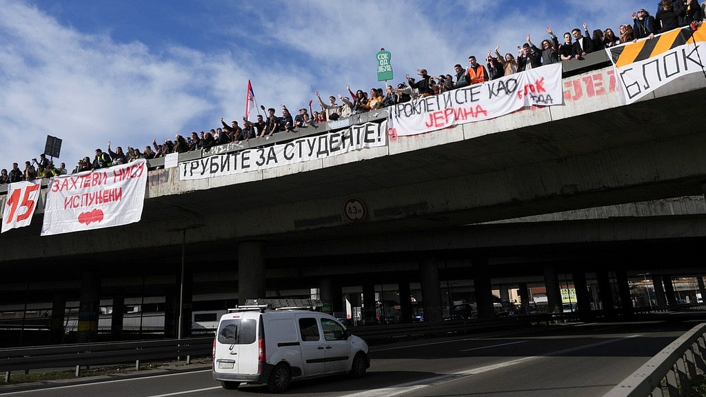 PTI : Students stand on a bridge during a student-led strike as they block an intersection for 24 hours to protest the deaths of 15 people killed in the November collapse of a train station canopy, in Belgrade, Serbia, Monday, Jan. 27, 2025. Writing on banners reads from left; "Requirement is not met”, "Honk for students", “You are damned like Damned Jerina”.