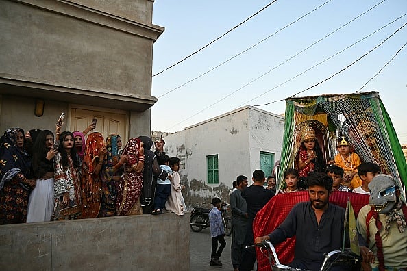 AFP via Getty Images : Hindu women watch the procession as they celebrate Hindu festival of Holi in Tharparkar district of the desert town of Mithi, south-eastern Pakistan, on March 13, 2025 |