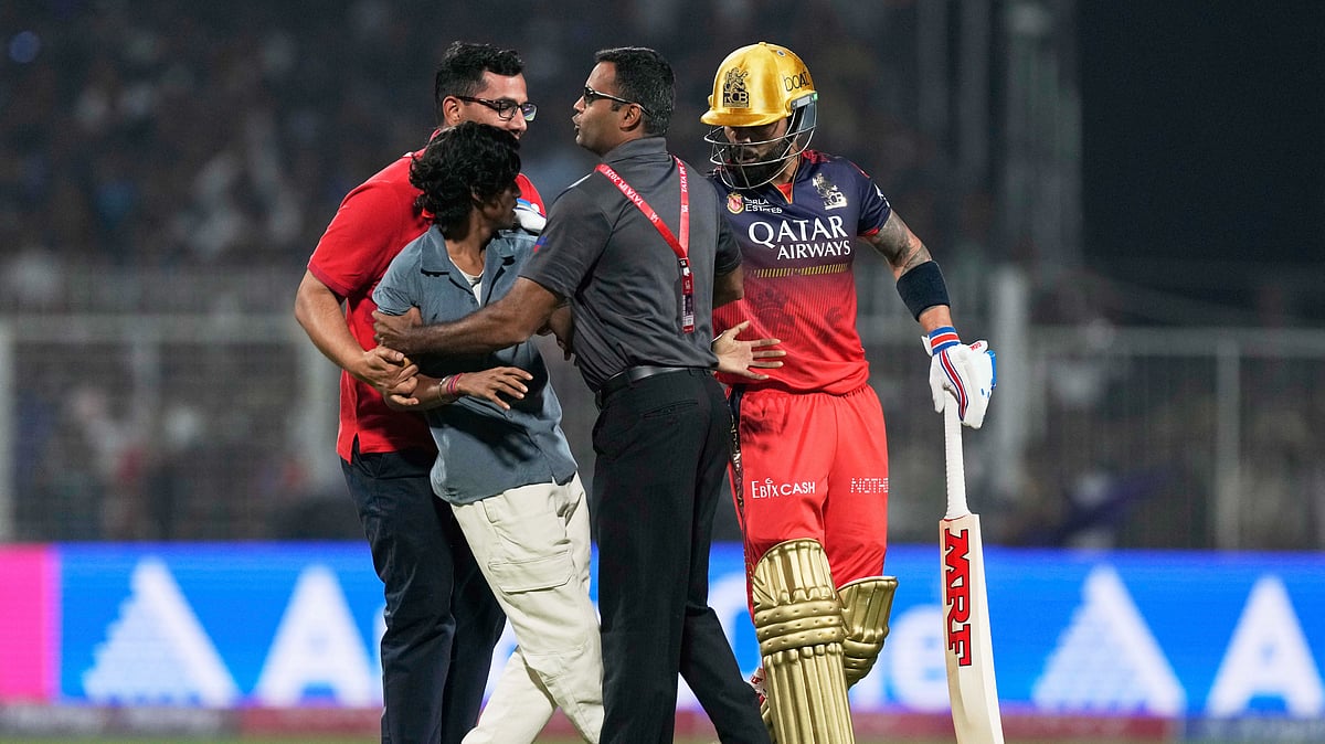 AP Photo/Bikas Das : Security personnel detain an intruder on the playing field as Royal Challengers Bengaluru's Virat Kohli looks on during the Indian Premier League cricket match between Kolkata Knight Riders and Royal Challengers Bengaluru at Eden Gardens in Kolkata.