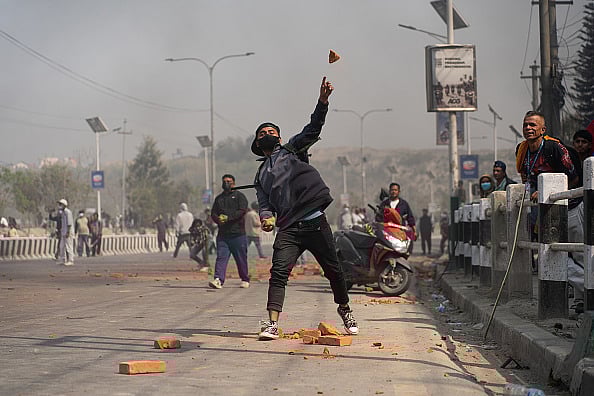 Photo by Rojan Shrestha/NurPhoto via Getty Images : A pro-monarchy protestor pelts stones at police personnel during a protest in Kathmandu, Nepal, on March 28, 2025.