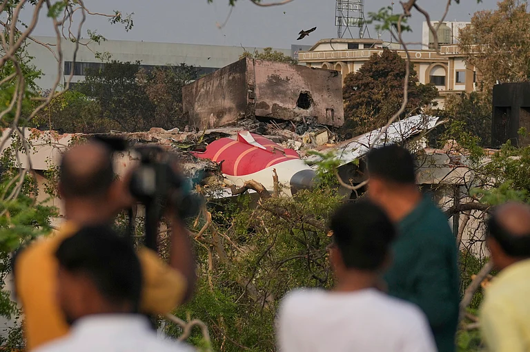 Onlookers watch wreckage from Thursday's Air India plane crash lying atop a building in Ahmedabad - Rafiq Maqbool/ AP