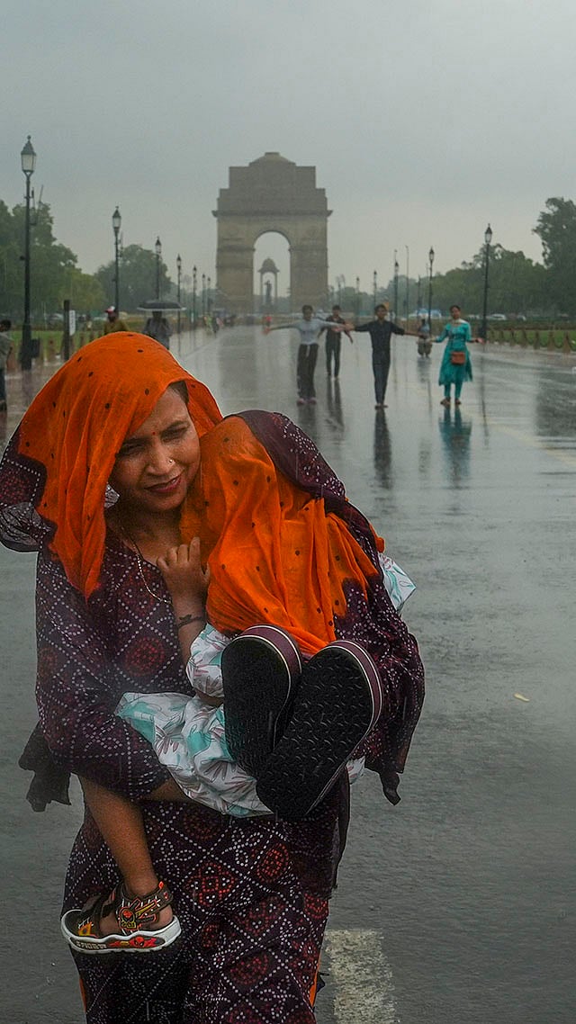 | Photo: PTI/Manvender Vashist Lav : A woman covers her child with a scarf during rain, at Kartavya Path, in New Delhi.