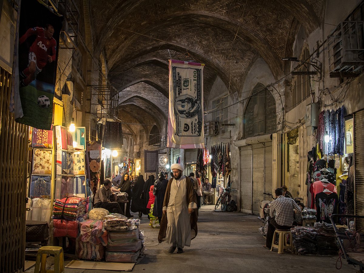 Shutterstock : Islam passing under a towel shaped like a US Dollar bill in the Isfahan bazar in the evening. The iranian rial, iran currency, is being devaluated facing the dollar