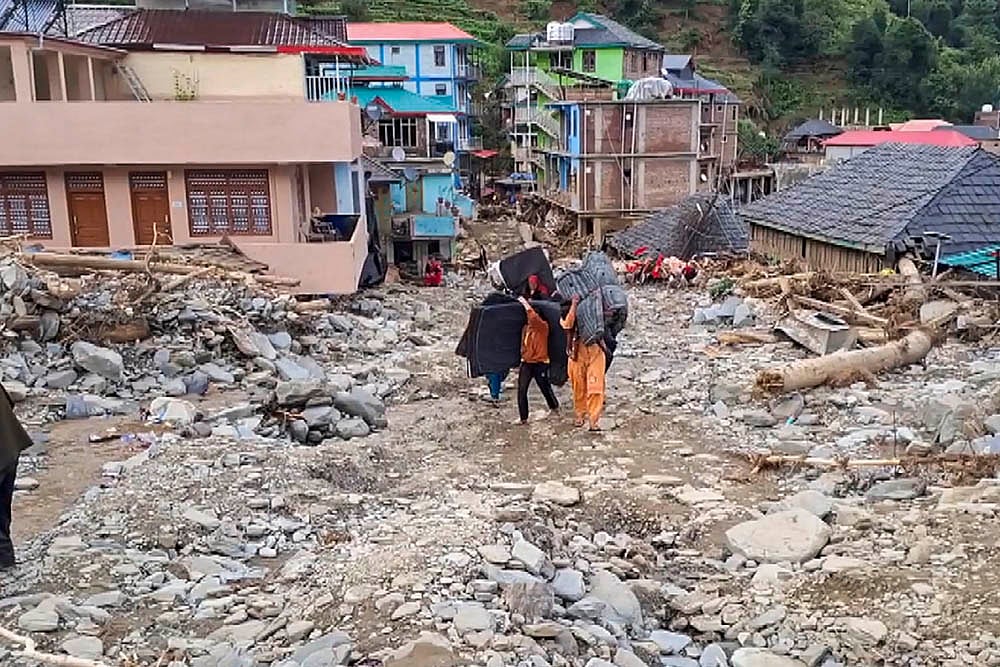 PTI : Locals carry their belongings as they walk amid the debris at a flood-affected area, at Thunag in Mandi district, Monday, July 7, 2025. 
