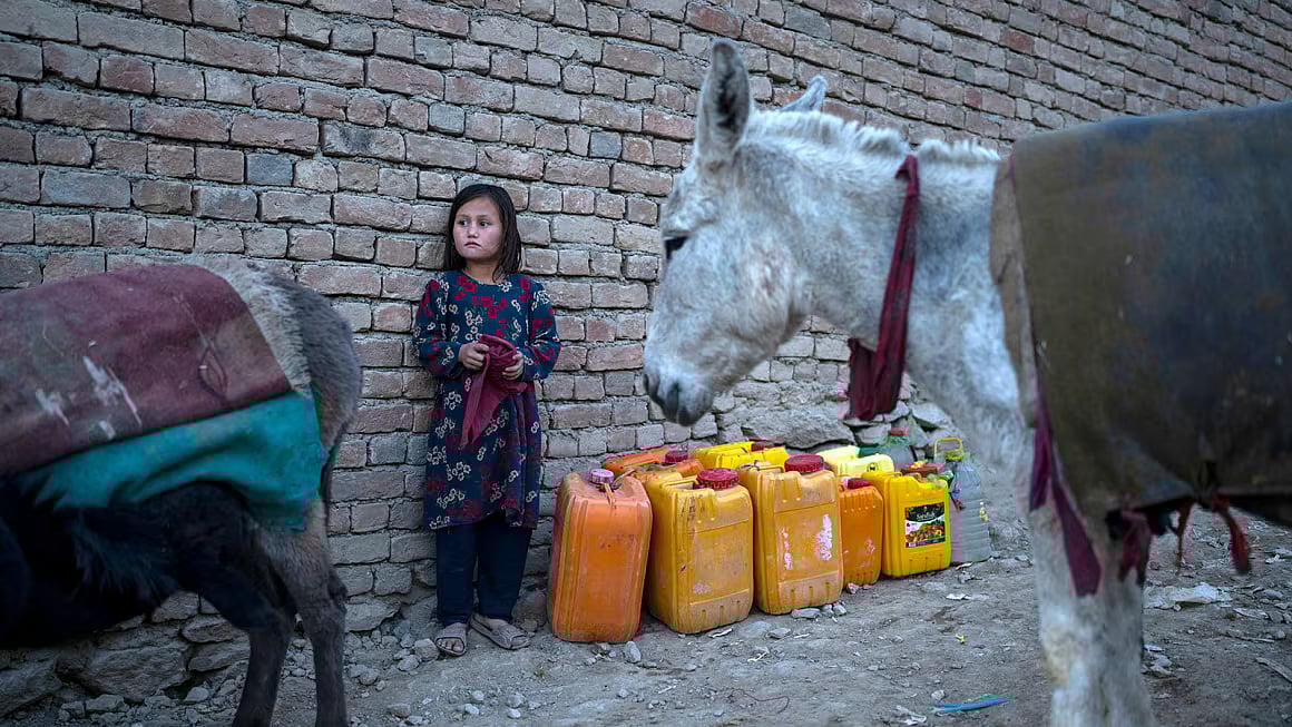 Petros Giannakouris/AP : An Afghan girl stands next canisters as she waits to fill them up with water in Kabul, Afghanistan, November 13, 2021