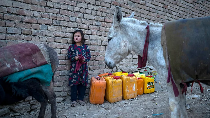 An Afghan girl stands next canisters as she waits to fill them up with water.