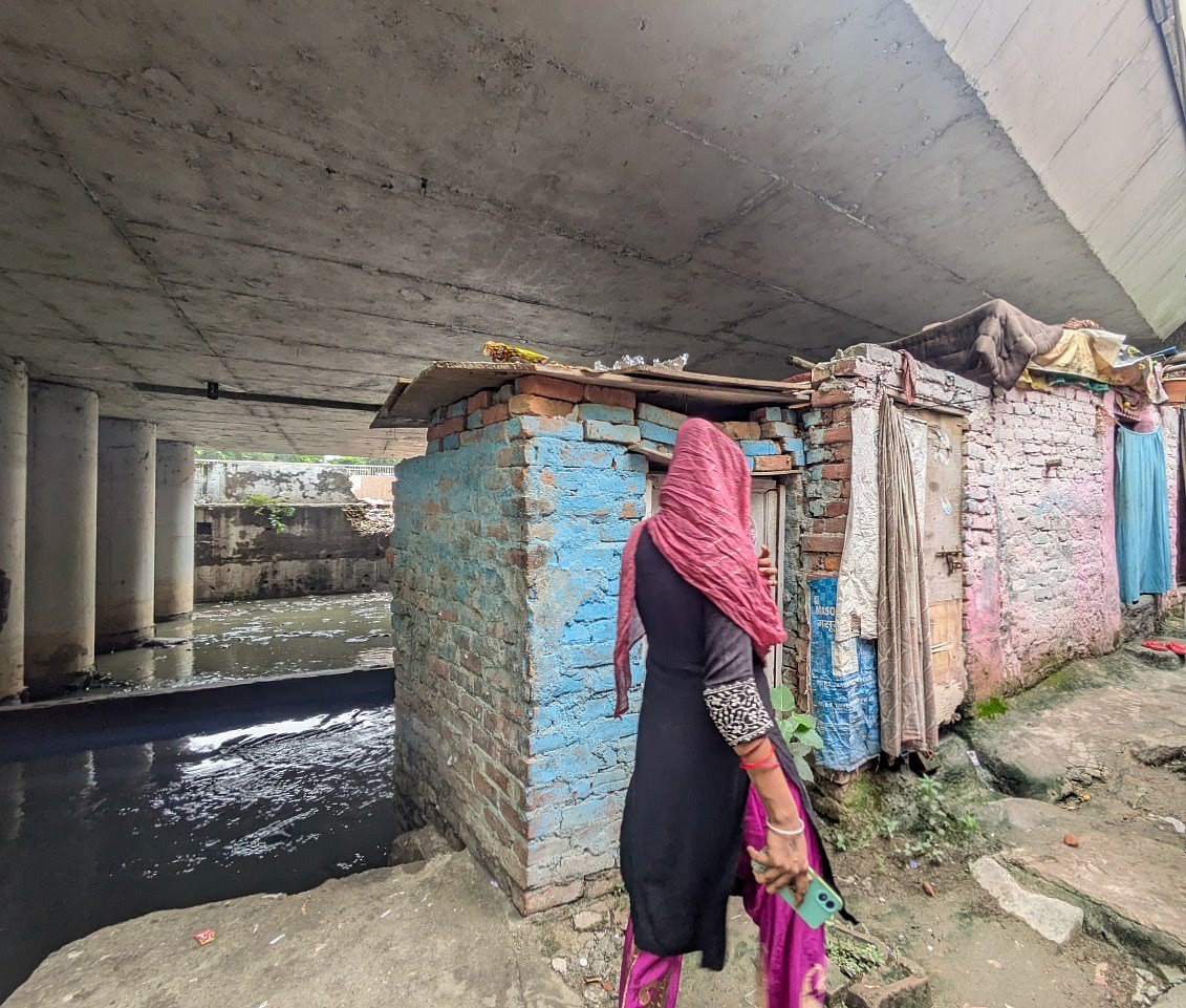 Saher Hiba Khan : A woman walks past shanties built under a flyover in Delhi’s Shaheed Arjun Das Camp. 
