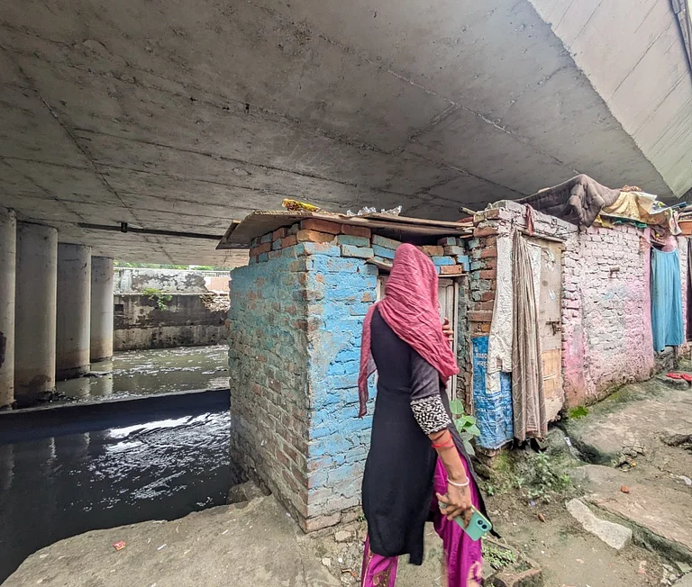 A woman walks past shanties built under a flyover in Delhi’s Shaheed Arjun Das Camp. - Saher Hiba Khan
