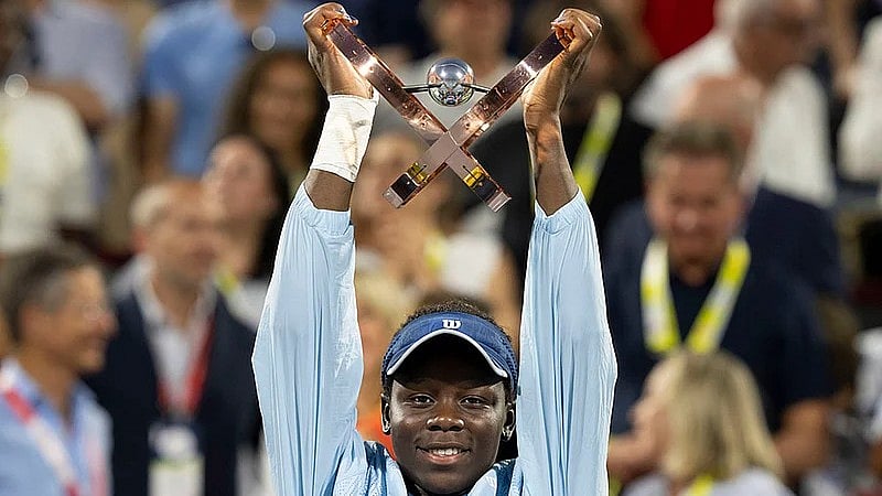 Christinne Muschi/The Canadian Press via AP : Victoria Mboko hoists the trophy following her win over Naomi Osaka in the Canadian Open final.