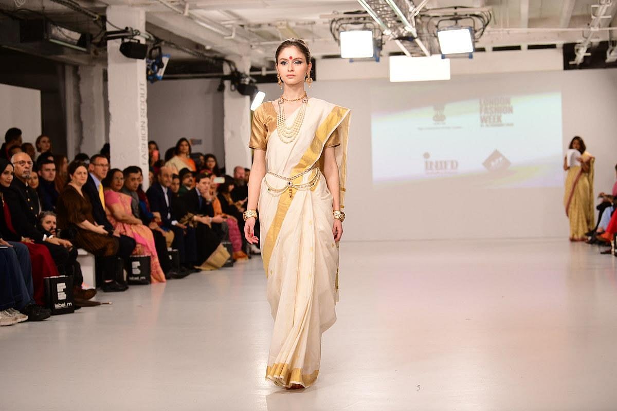 Model walking the runway in a traditional white and gold saree during a fashion show