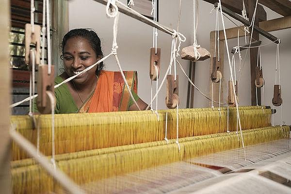 A woman in a saree weaving fabric on a traditional handloom.