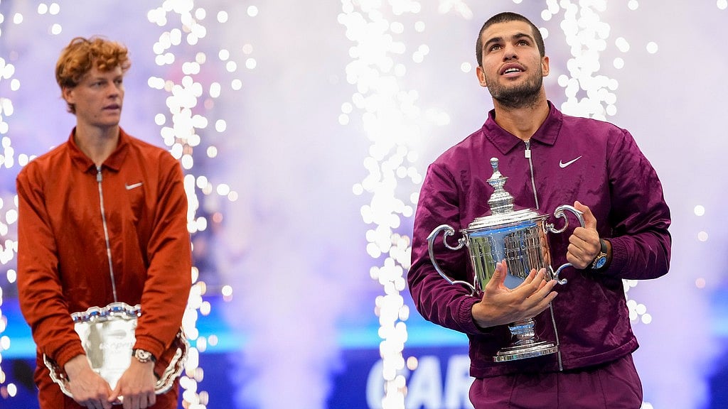AP : Carlos Alcaraz, of Spain, holds the championship trophy as Jannik Sinner, of Italy, looks on after Alcaraz defeated Sinner in the men's singles final of the US Open.