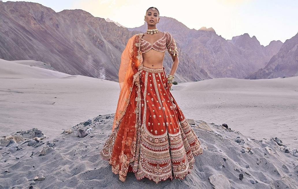 A woan in a chaniya choli dress standing in a rocky, mountainous landscape.