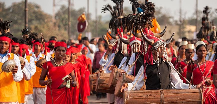 A vibrant tribal procession with people in orange robes and a decorated chariot