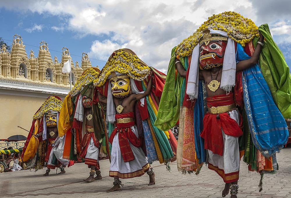 Three dancers in colorful, ornate costumes and masks perform in a procession.