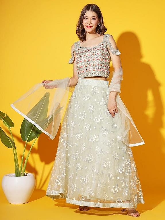 Woman wearing a white embroidered lehenga, standing against a yellow background
