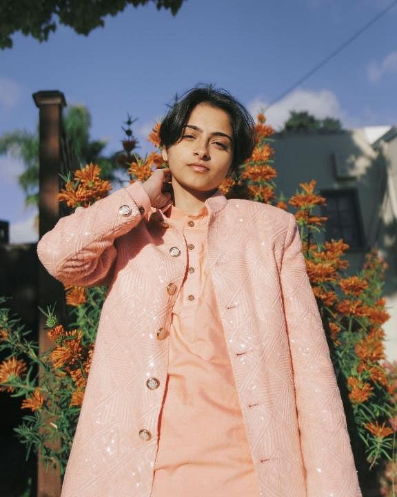 A person with dark hair wears a light pink layered outfit.