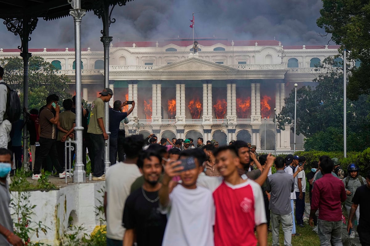 AP Photo/Niranjan Shrestha : Protesters take selfies and celebrate at the Singha Durbar, the seat of Nepal's government's various ministries and offices, after it was set on fire during a protest against social media ban and corruption in Kathmandu, Nepal, Tuesday, Sept. 9, 2025. 