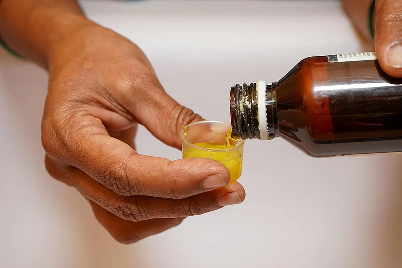 A person pouring cough syrup into a measuring cup