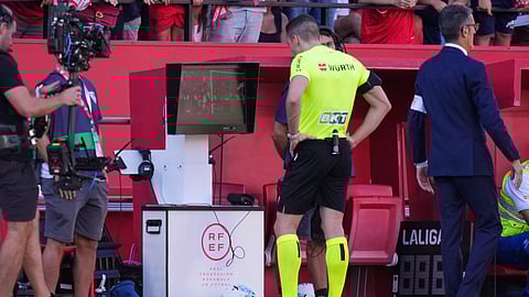 Referee Alejandro Muniz Ruiz pauses the match and checks the VAR screen during the Spanish La Liga soccer match between Sevilla and Barcelona at the Ramon Sanchez Pizjuan stadium in Seville, Spain, Sunday, Oct. 5, 2025. 