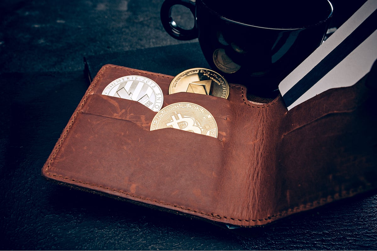 Close-up of an open brown leather wallet with several physical crypto coins.