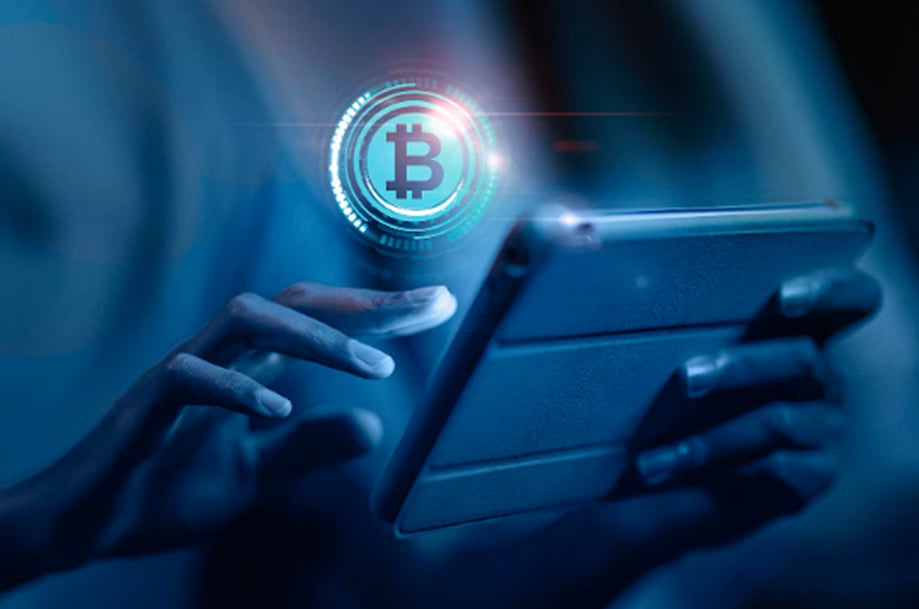 A person holding a tablet under blue light with a glowing Bitcoin symbol overlay.