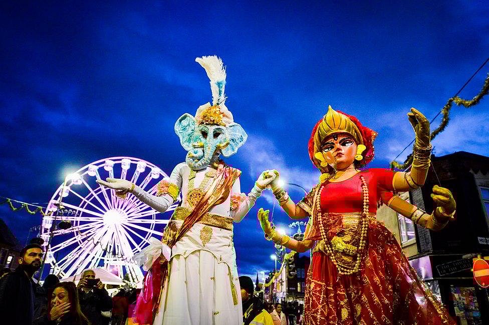 Large figures of Hindu deities at a Diwali parade with a Ferris wheel.