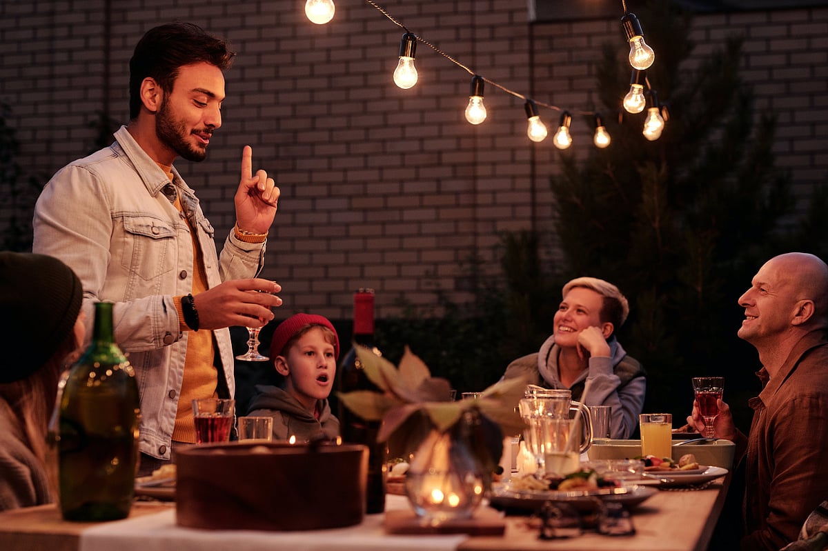 A man telling a story to friends gathered at an outdoor dinner table under string lights.