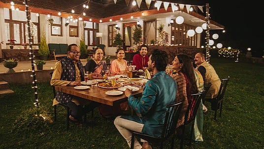 A group of friends or family enjoying a Diwali dinner party outdoors under string lights.