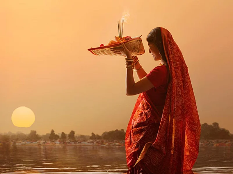Women performing Chhath Puja ritual in water with a puja thali during sunset