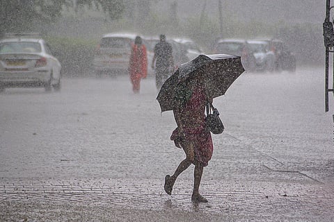 A woman makes her way through a rain-soaked road during rainfall, in Thane, Maharashtra.