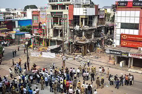 Police and security personnel stand guard as locals gather on a street following action against illegal construction at Central Market Complex, in Meerut. The Housing Development Council announced the move after a Supreme Court order, prompting traders to vacate the area. 