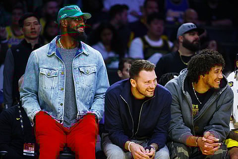 Los Angeles Lakers forward LeBron James (23) and Los Angeles Lakers guard Luka Doncic (77) watch from the bench during the second half of an NBA basketball game against the Portland Trail Blazers in Los Angeles.