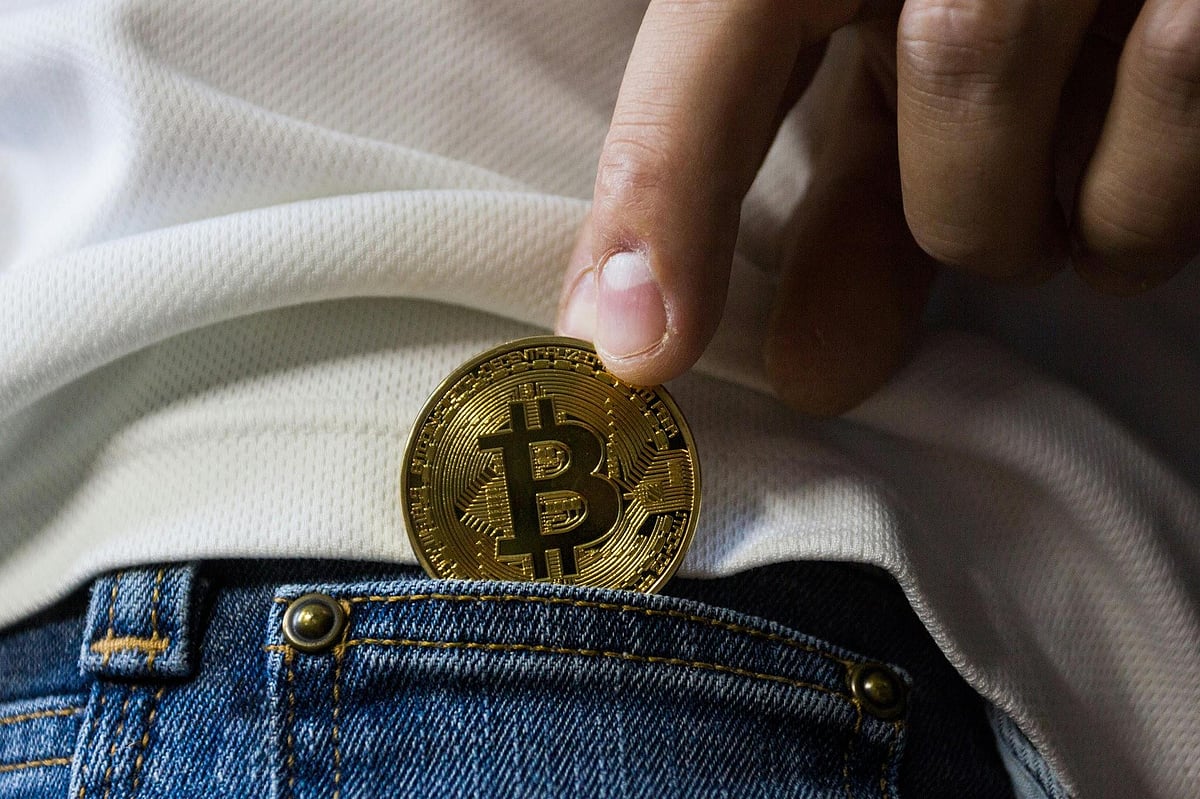 A hand putting a gold bitcoin into the front pocket