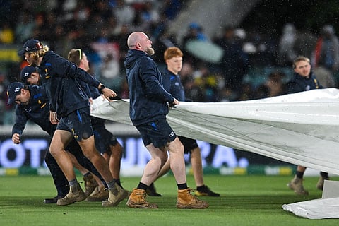 Ground staff pull the covers over the pitch as rain stops play during the T20 cricket international between India and Australia in Canberra, Australia.