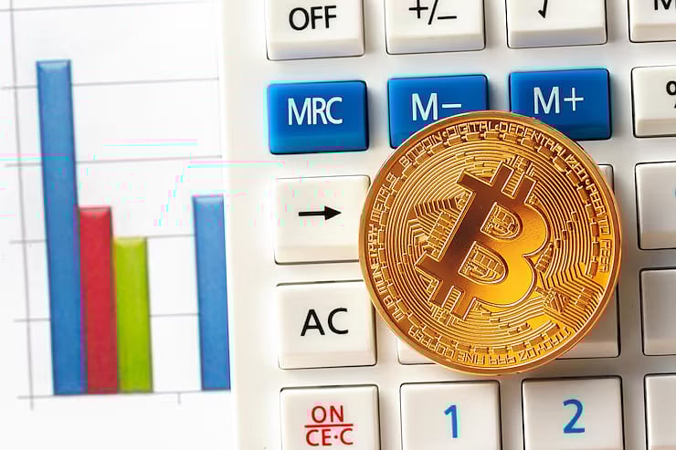 A gold Bitcoin coin rests on a calculator next to a digital bar chart graphic.
