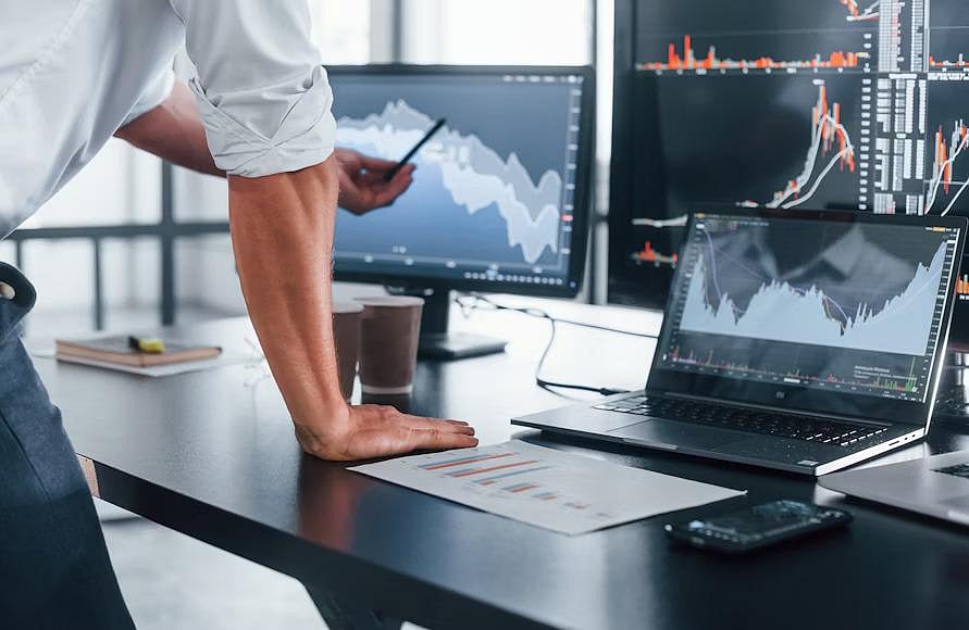 Person analyzing crypto charts on multiple monitors in a modern office setup.