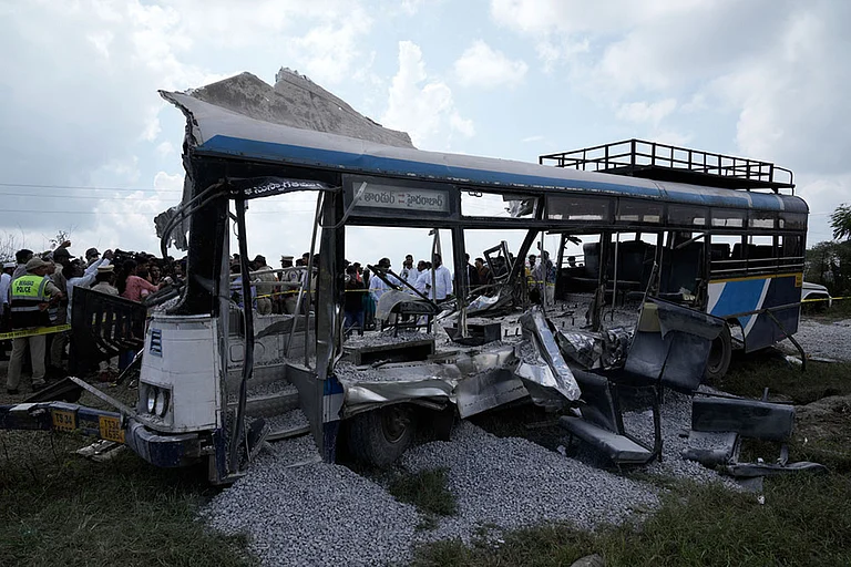 People stand next to the passenger bus after a truck loaded with concrete stone chips rammed into it at Chevalla in southern state of Telangana, India. - | Photo: AP/Mahesh Kumar A.