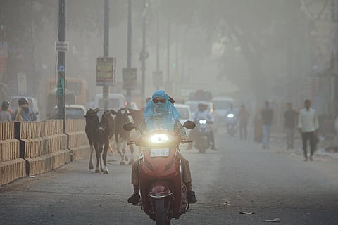 A woman rides a scooter amid low visibility due to a thick layer of smog, in Gurugram.