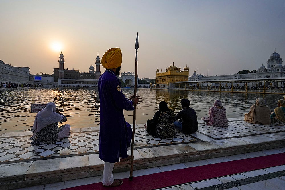People sit near 'Amrit Sarovar' at the Golden Temple on the occasion of Guru Nanak Jayanti, in Amritsar. - | Photo: PTI/Shiva Sharma
