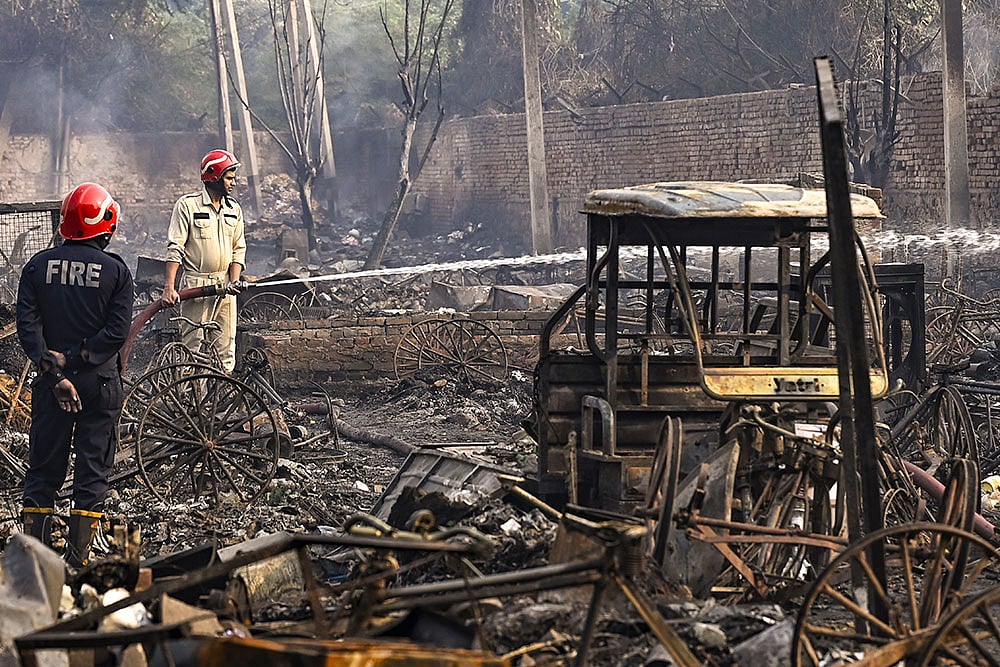 | Photo: PTI : New Delhi: Firemen spray water on charred remains after a fire broke out spreading to around 500 shanties near Rithala metro station, at Rohini area, in New Delhi. Police said several LPG cylinders were said to have exploded late Friday evening, intensifying the blaze and triggering panic among residents. 