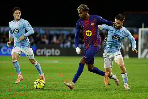 Barcelona's Lamine Yamal, center, passes the ball challenged by Celta's Sergio Carreira, right, during the Spanish La Liga soccer match between Celta Vigo and Barcelona in Vigo, Spain.