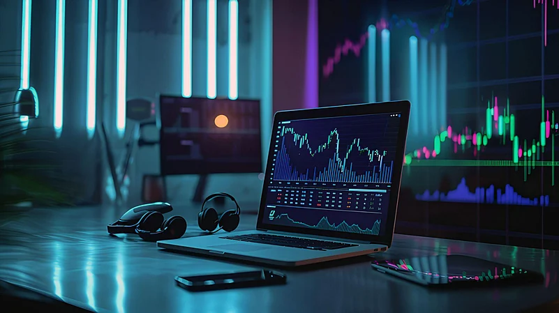 A laptop showing crypto trading charts in a blue-lit tech workspace