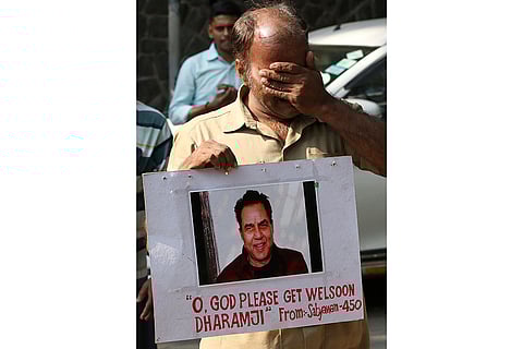A fan of Bollywood actor Dharmendra gets emotional as he holds a poster praying for the recovery of the veteran actor, outside his bungalow in Mumbai.