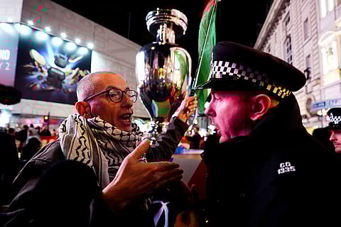 A protester speaking with a police officer near a replica UEFA trophy during the Euro 2028 launch at Below The Lights, Piccadilly Circus, London.