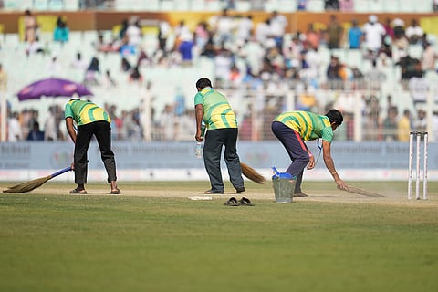 Groundsmen use brooms to remove dust from the pitch during the lunch break on the third day of the first cricket test match between India and South Africa in Kolkata, India.