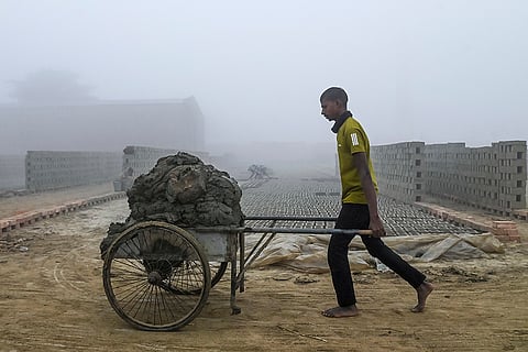A worker pushes a wheelbarrow loaded with clay at a brick kiln on a winter morning, in Nadia.