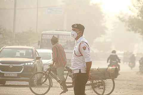 A traffic police personnel wears a mask while managing traffic amid low visibility as the air quality deteriorates, in Gurugram.